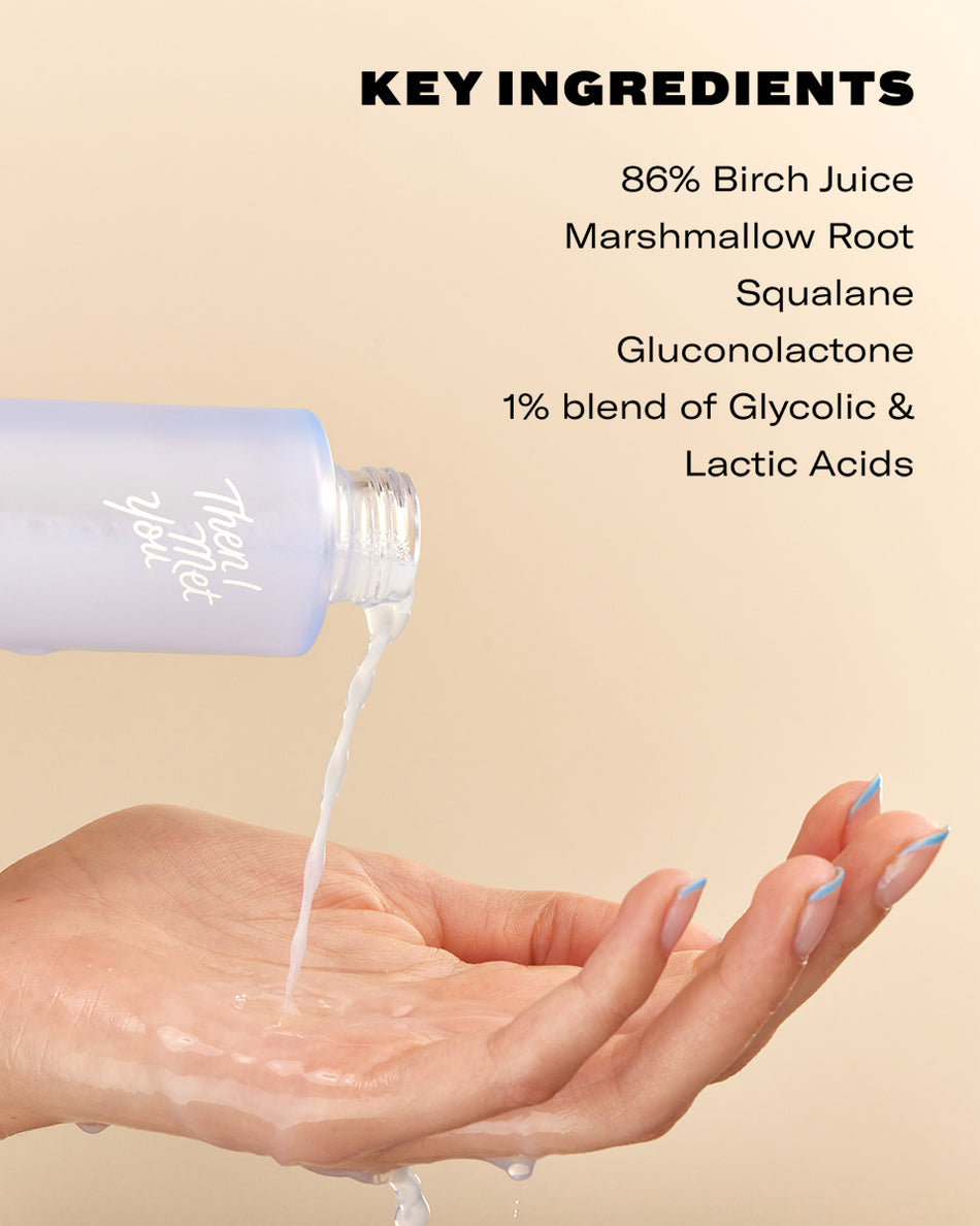 Clear liquid being poured from a light purple bottle onto an open hand with manicured nails against a beige background with.