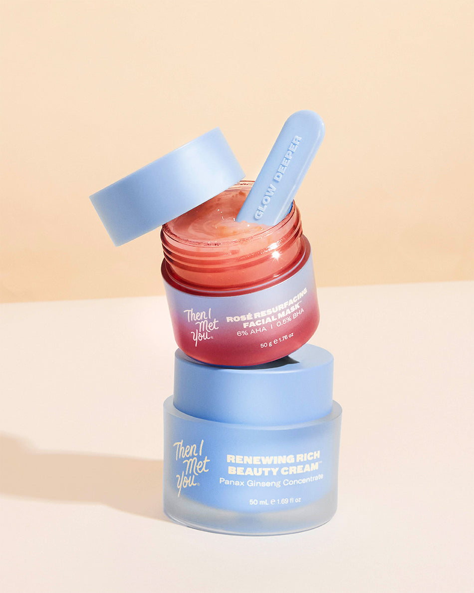 Two stacked skincare jars with blue lids, one open showing pink cream and a blue spatula inside.