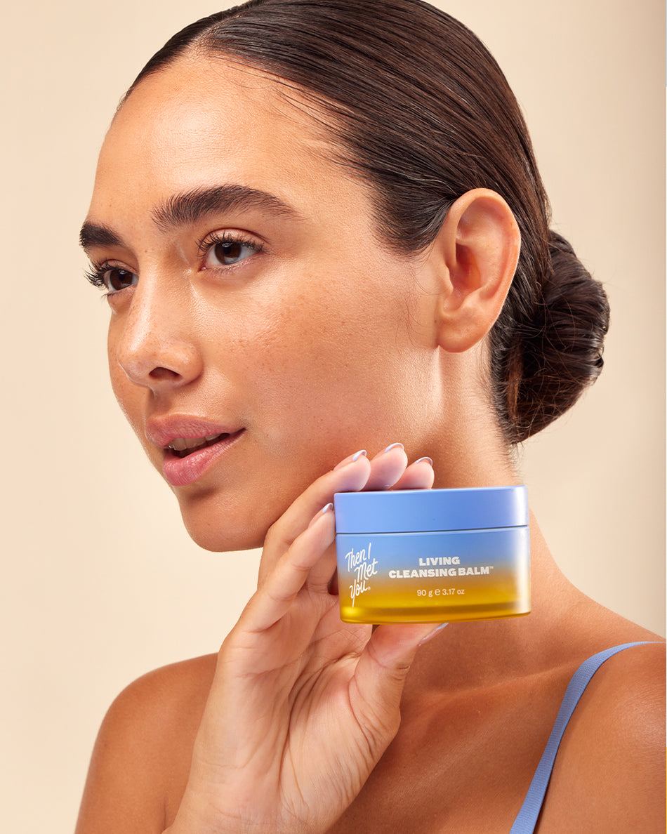 Woman with sleek bun holding Living Cleansing Balm jar with blue and yellow label.