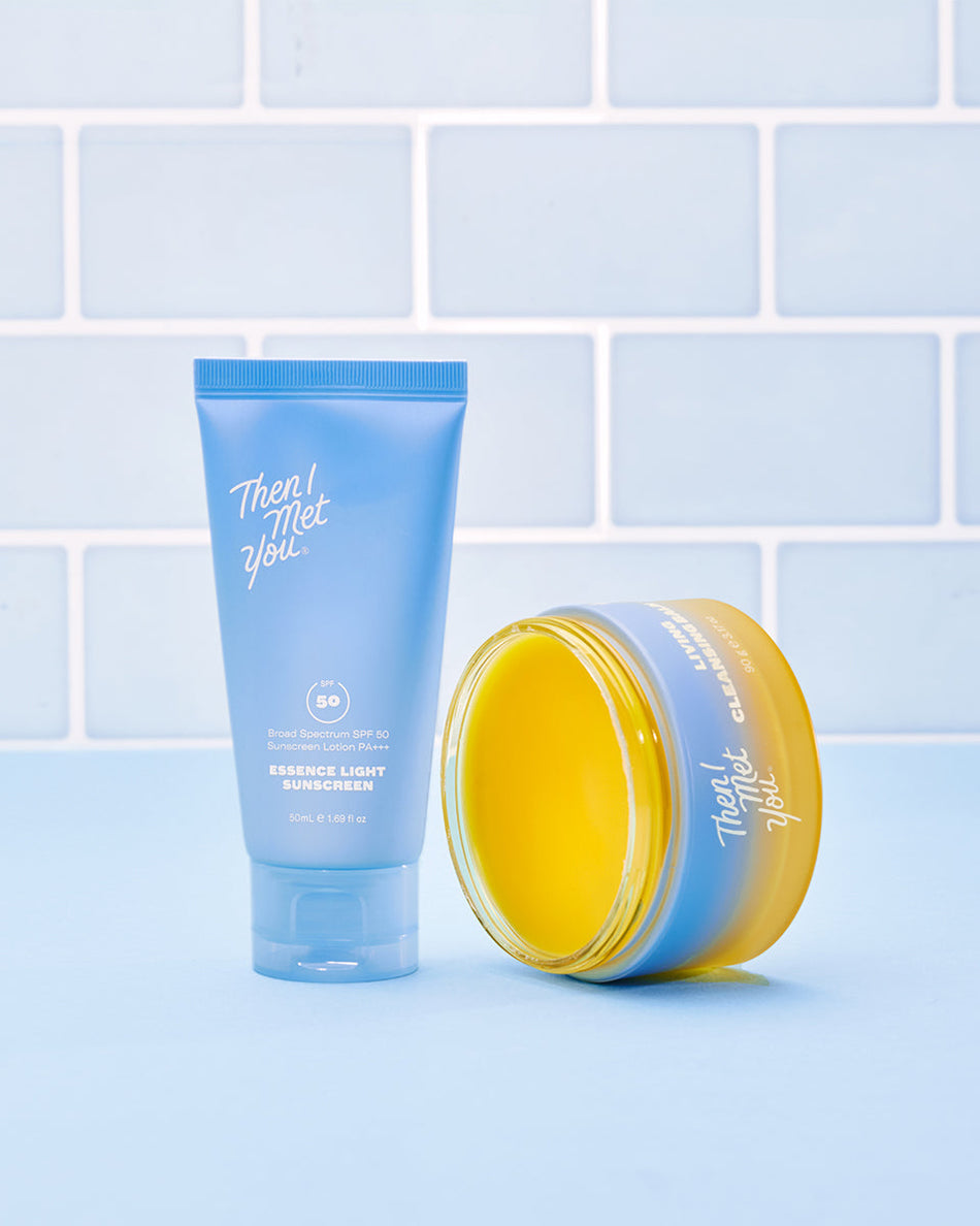 Blue tube of protective skincare cream beside open yellow jar of purifying balm on light blue surface with tiled background.