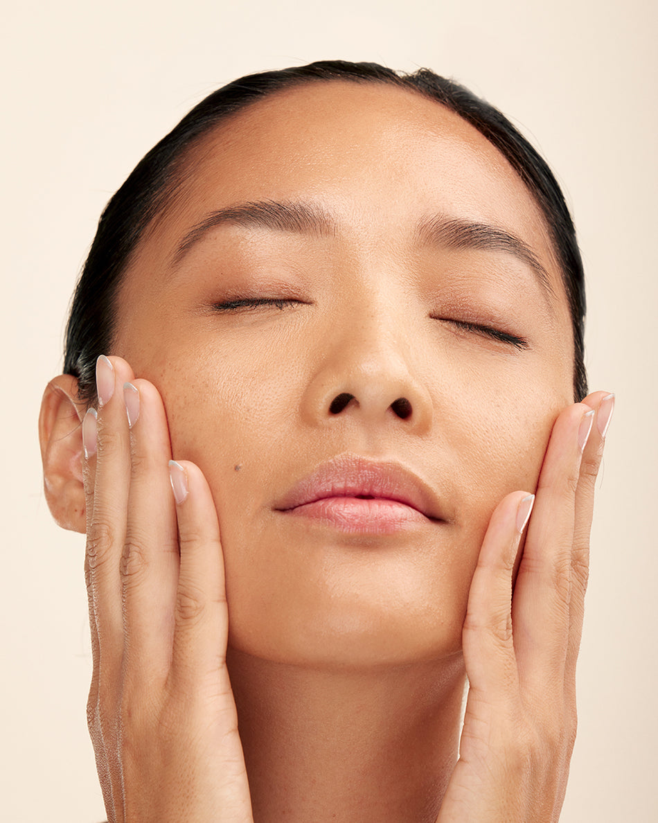 Woman with closed eyes gently touching her smooth skin, highlighting natural glow.