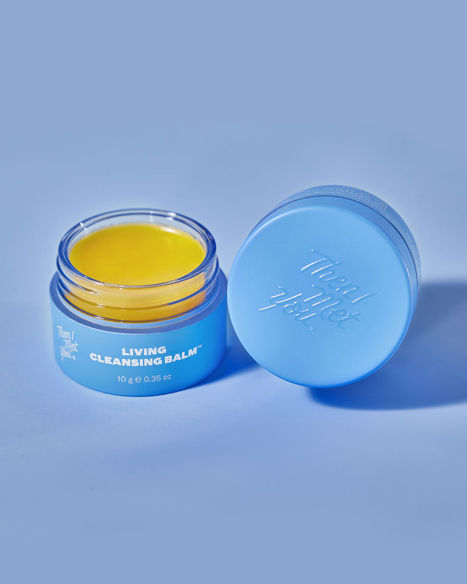 Open blue jar of yellow cleansing balm with matching blue lid on light blue background.