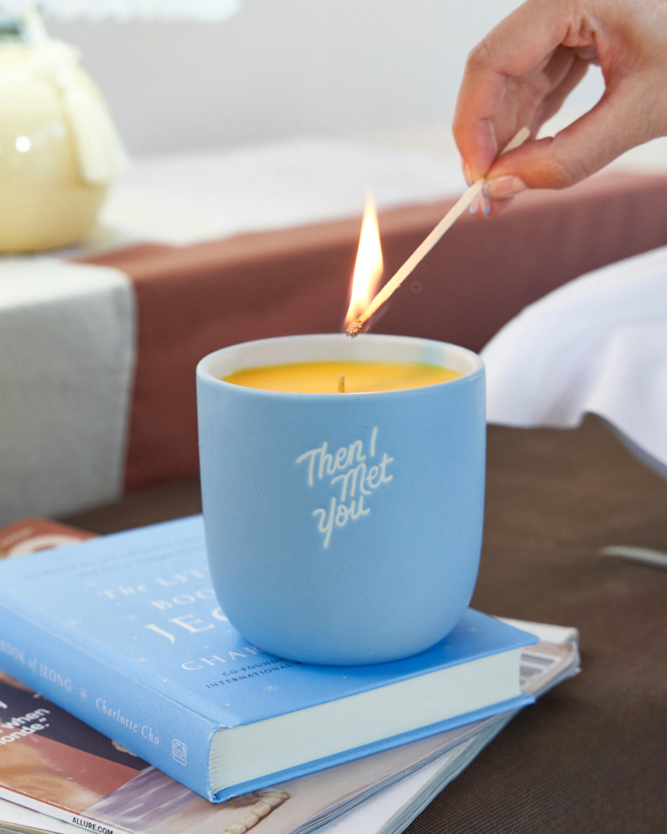Blue ceramic candle cup with "Then I Met Yvette" text, lit yellow wax candle inside.