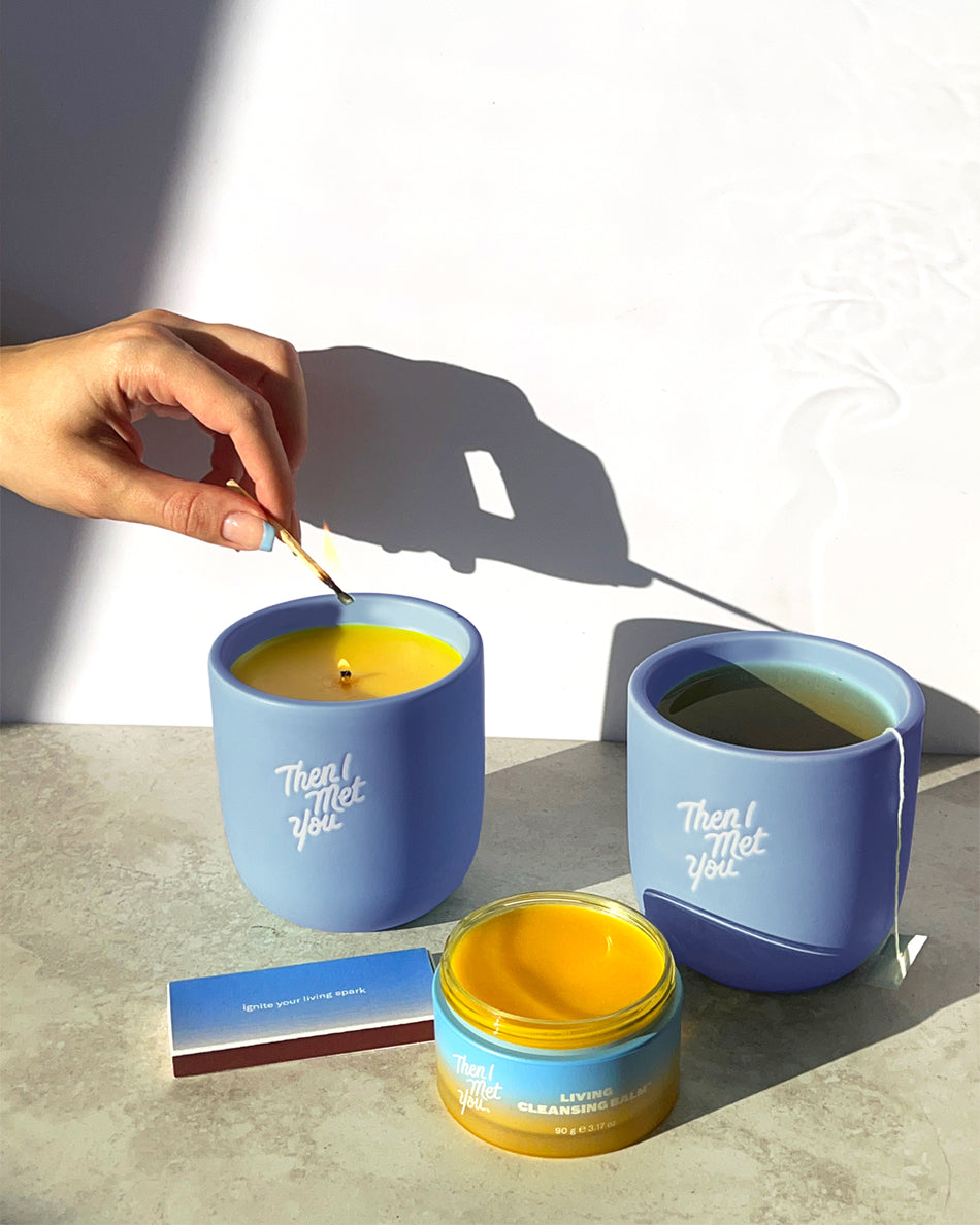 Blue ceramic scented candle labeled "That Glow" with wooden wick and accompanying blue ceramic mug on gray surface.