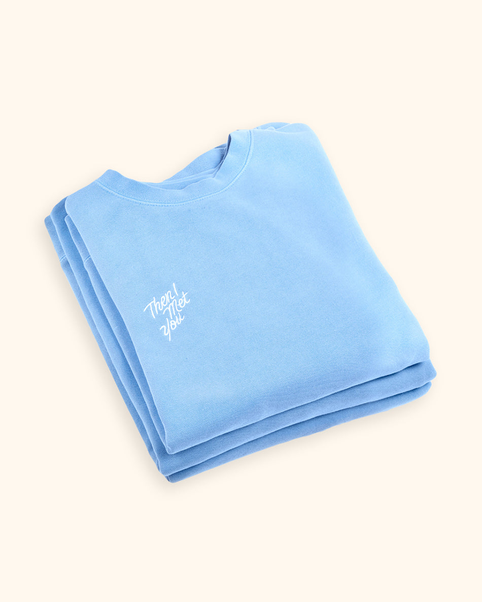 Folded periwinkle blue cotton pullover with small white embroidered logo on chest.